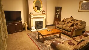 A living room with a fireplace, sofa, coffee table, and television. - Manor House Hotel Cockermouth (Cockermouth)