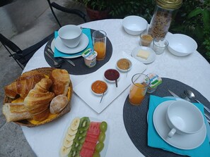 A round table with breakfast items including croissants, fruit, and beverages, surrounded by plates and cutlery. - Chambres d'Hotes O Anges (Arles)