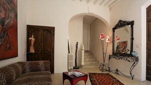 A living room with a leopard print sofa, a red side table, a patterned rug, a staircase, and a mirror with a decorative frame. - Chambres d'Hotes O Anges (Arles)