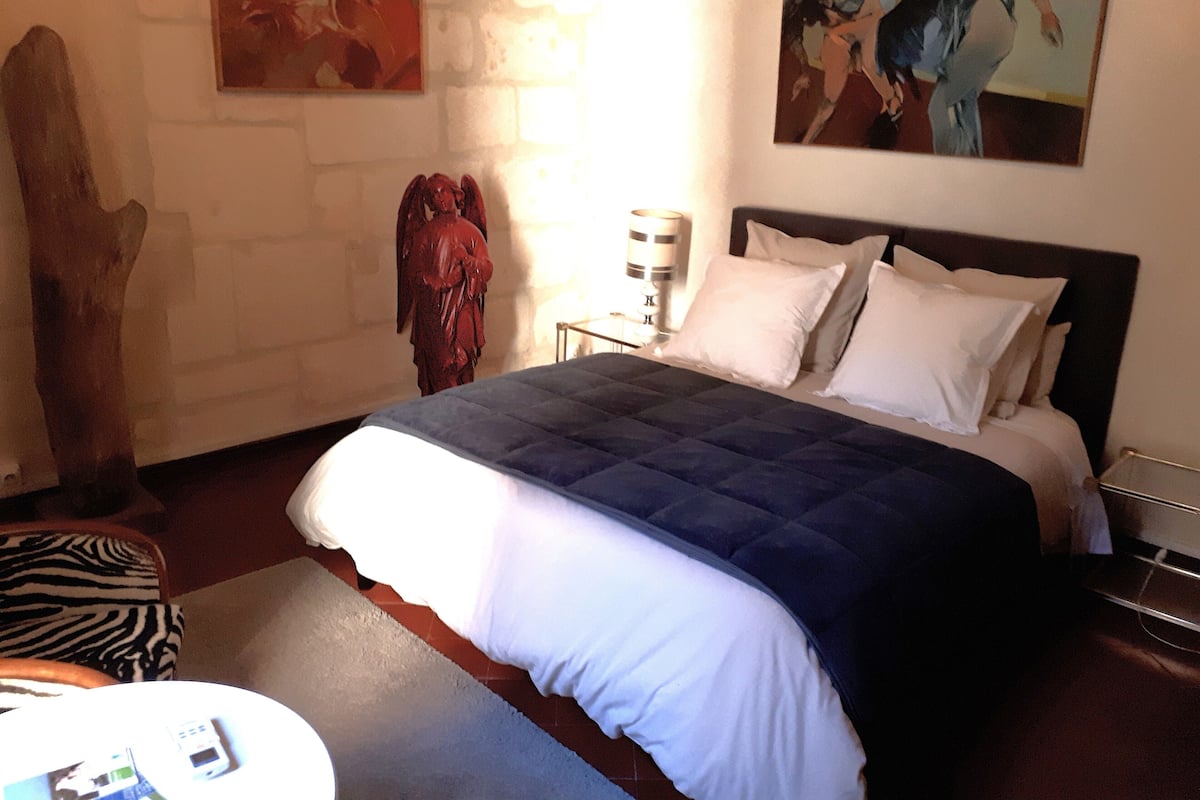 A bedroom with a bed, a nightstand, a lamp, and a painting on the wall.