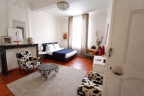 A hotel room with a bed, a desk, a chair, a small table, a mirror, and a chandelier. - Chambres d'Hotes O Anges (Arles)