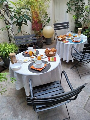 A table set for breakfast with plates, cups, and a basket of pastries. - Chambres d'Hotes O Anges (Arles)