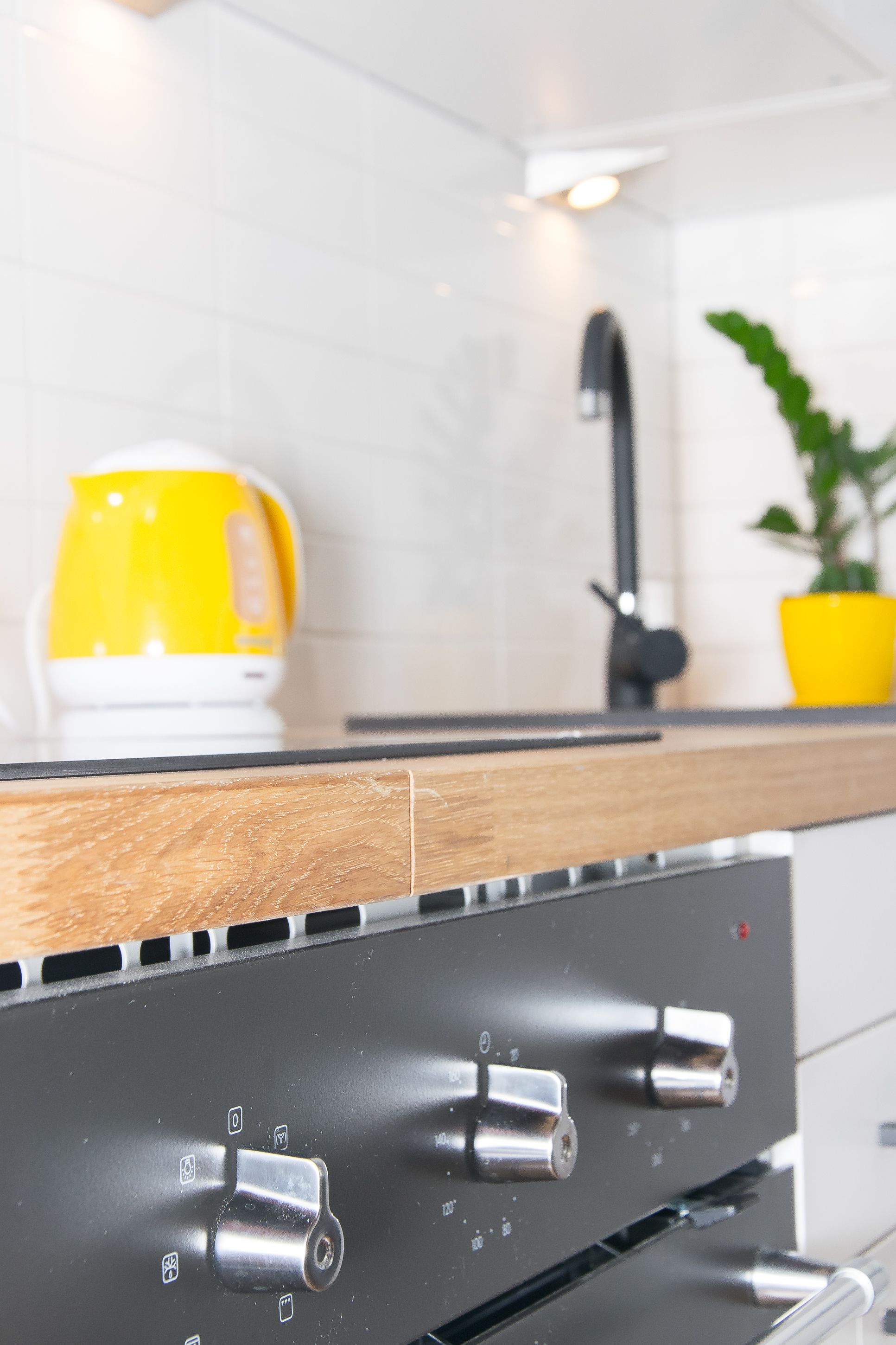 A kitchen with a wooden countertop, a yellow kettle, a black faucet, and a potted plant.