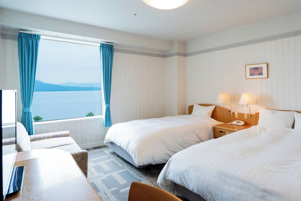 A hotel room with two beds, a desk, and a view of the sea.