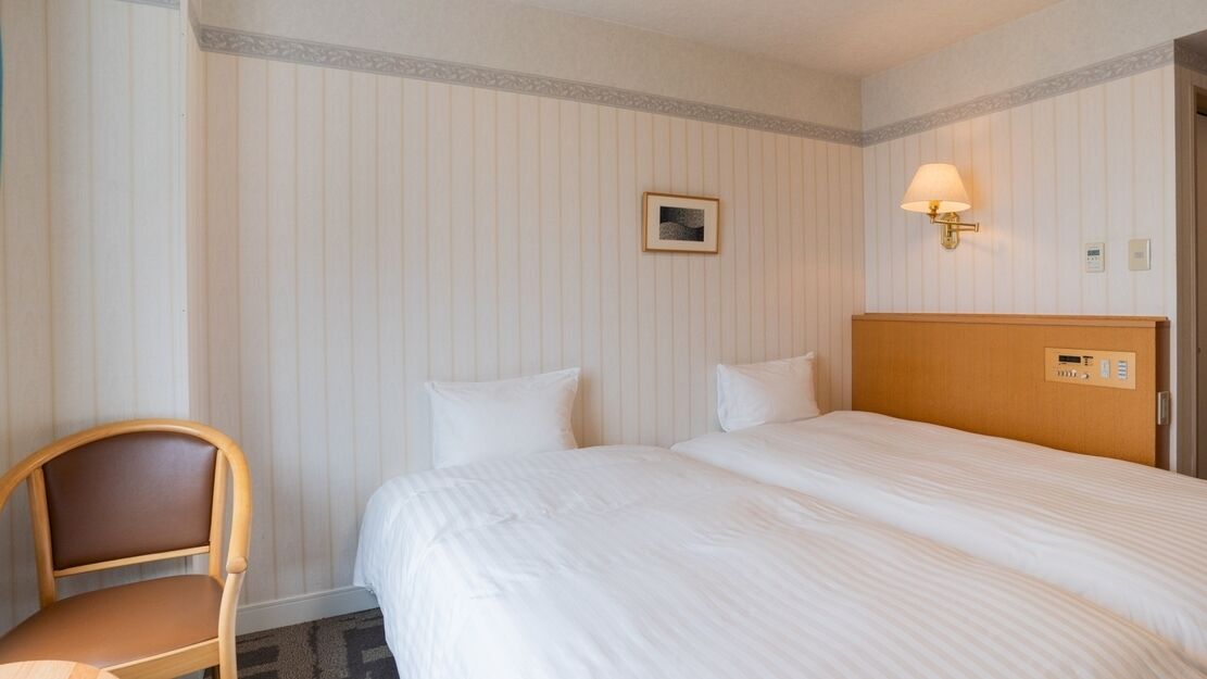 A hotel room with a bed, a chair, a wall-mounted lamp, and a small picture frame.