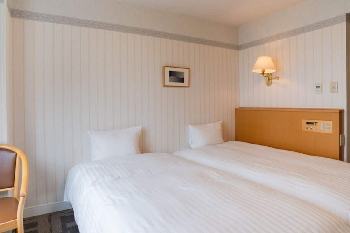 A hotel room with a bed, a chair, a wall-mounted lamp, and a small picture frame.