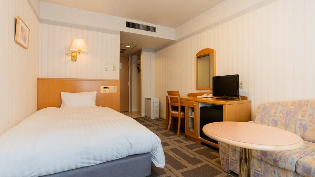 A hotel room with a bed, a desk with a computer, a chair, a small table, and a sofa.