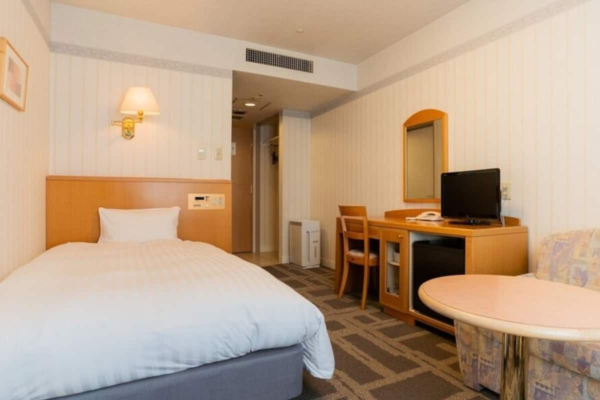 A hotel room with a bed, a desk with a computer, a chair, a small table, and a sofa.