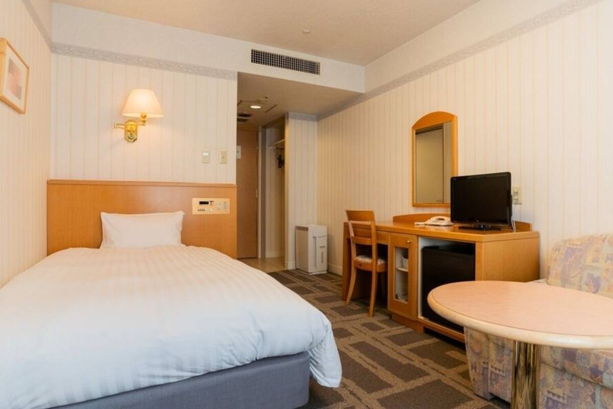 A hotel room with a bed, a desk with a computer, a chair, a small table, and a sofa.