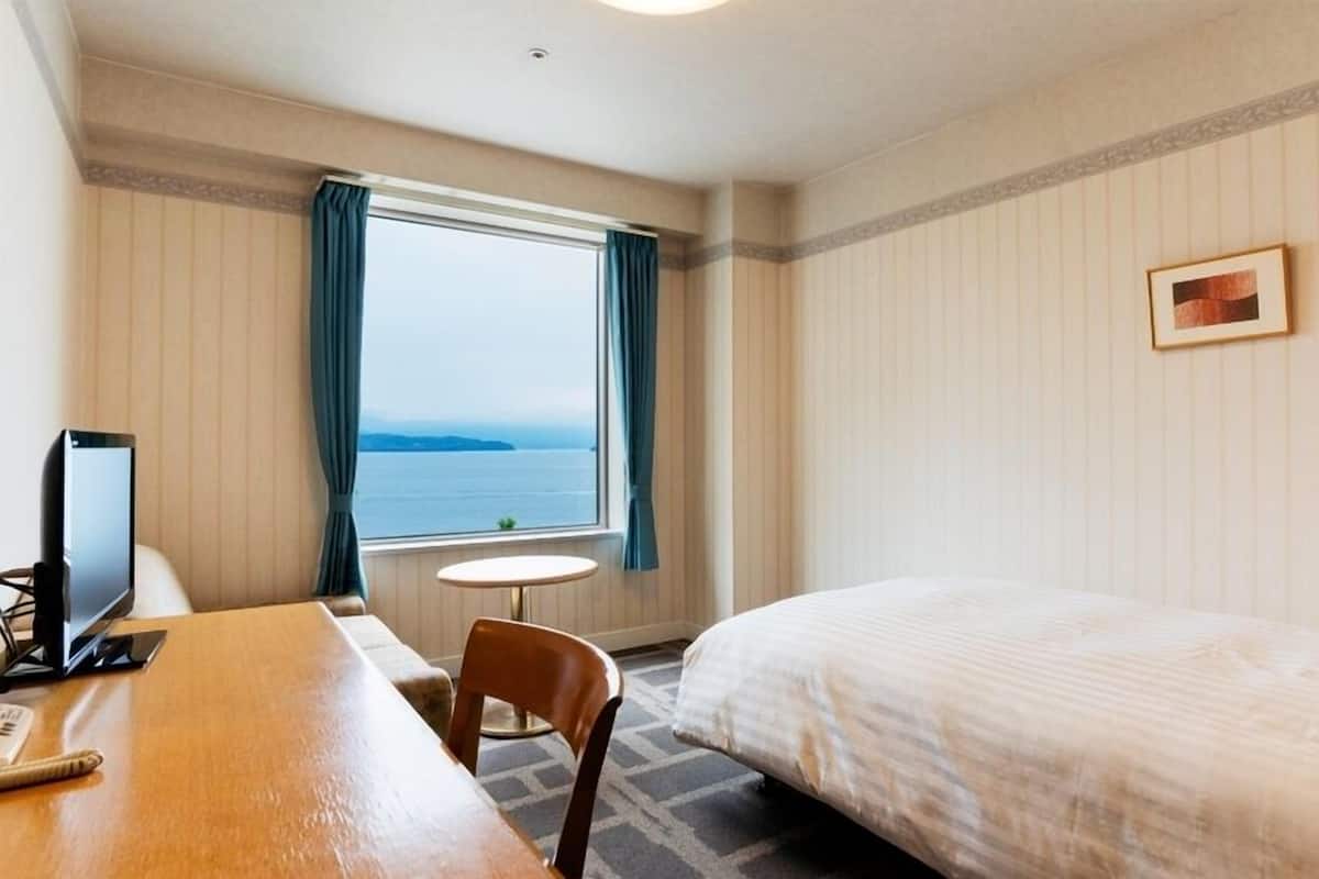 A hotel room with a bed, a desk with a computer, a small table, and a window with curtains.