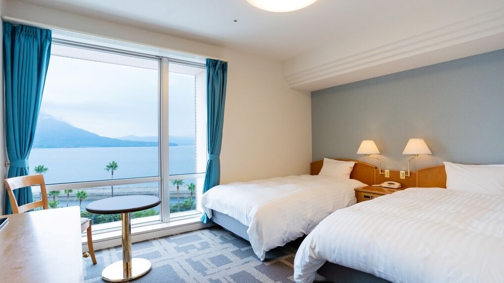 A hotel room with two beds, a small table, and a view of the sea.