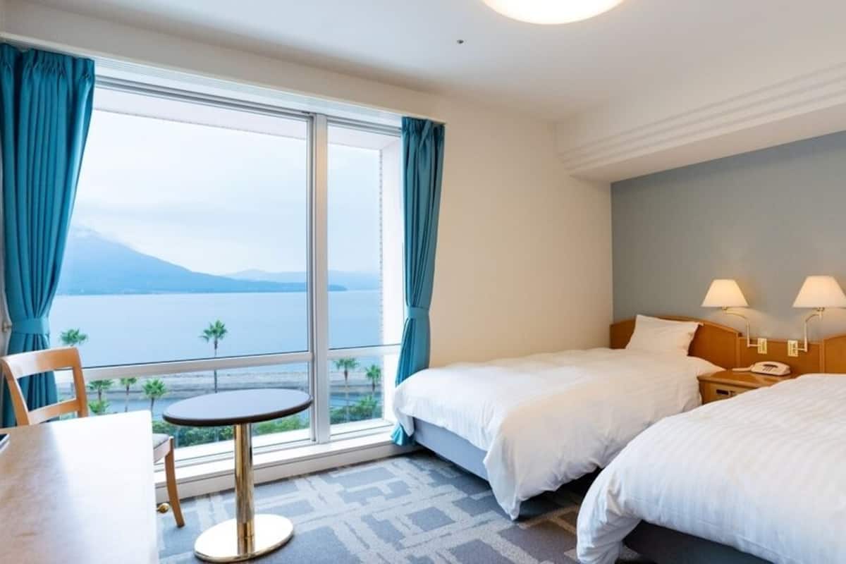 A hotel room with two beds, a small table, and a view of the sea.