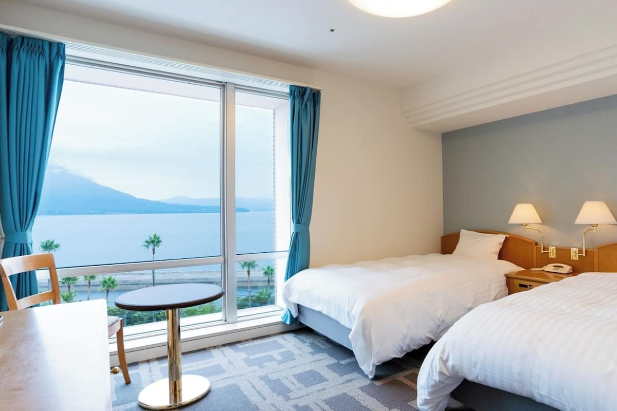 A hotel room with two beds, a small table, and a view of the sea.