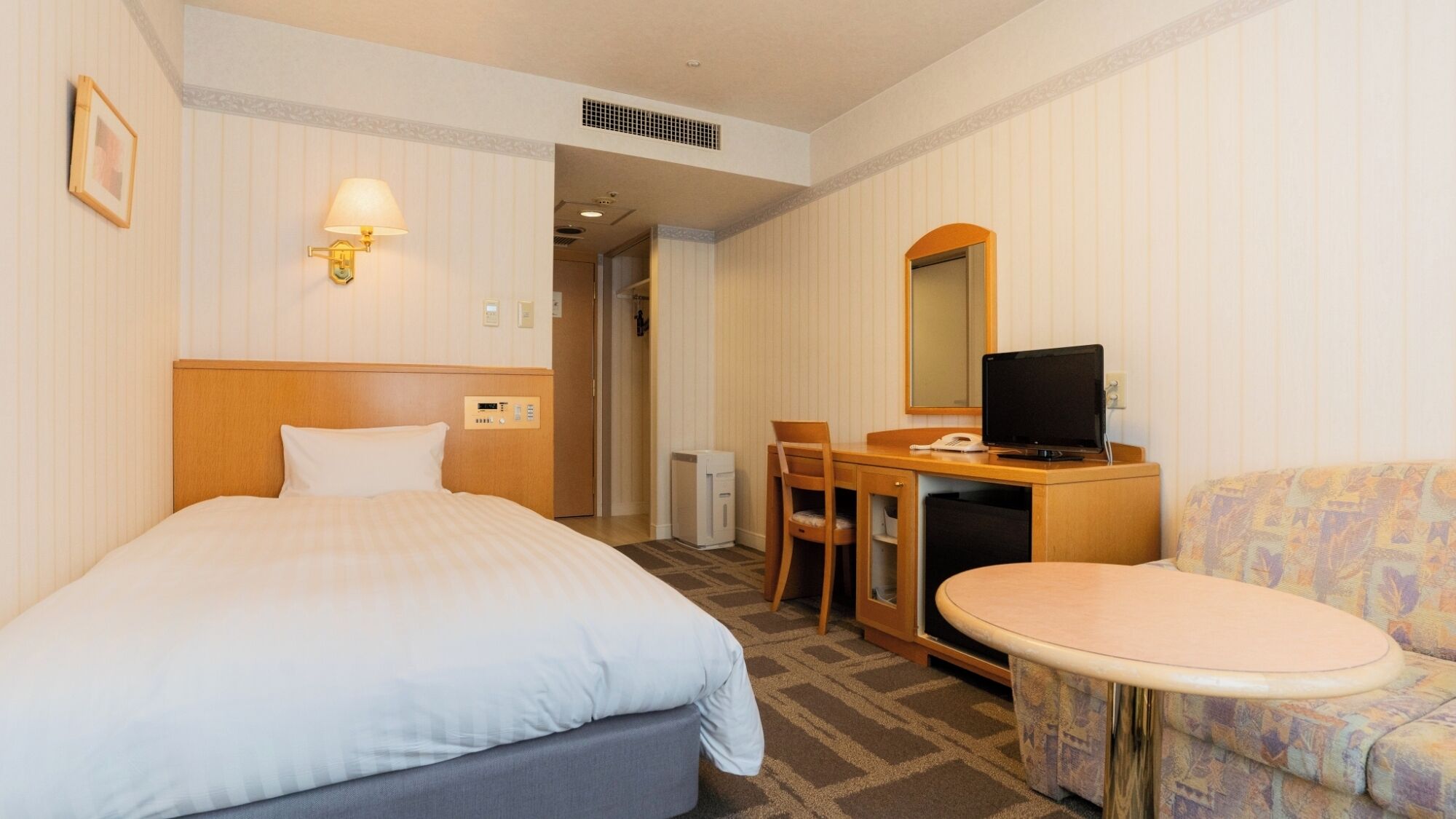 A hotel room with a bed, a desk with a computer, a chair, a small table, and a sofa.