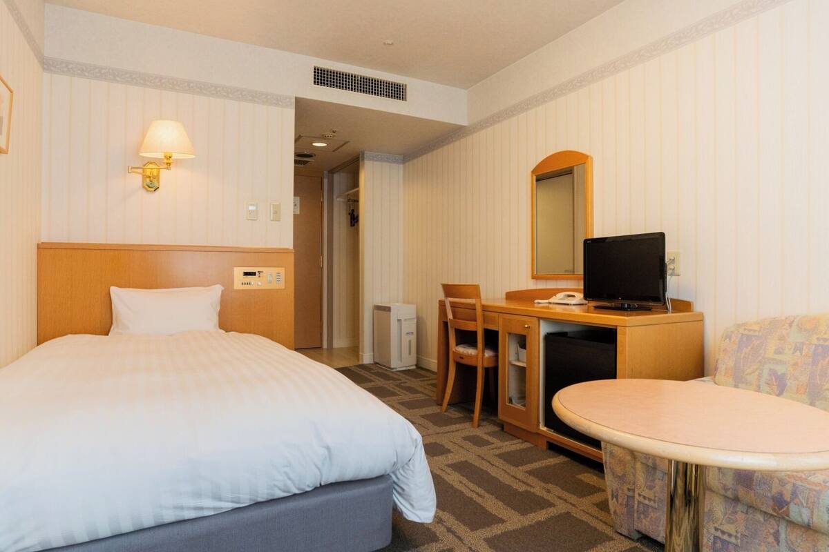 A hotel room with a bed, a desk with a computer, a chair, a small table, and a sofa.