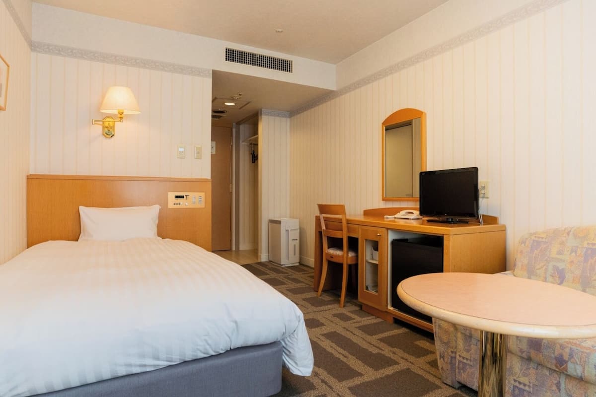 A hotel room with a bed, a desk with a computer, a chair, a small table, and a sofa.