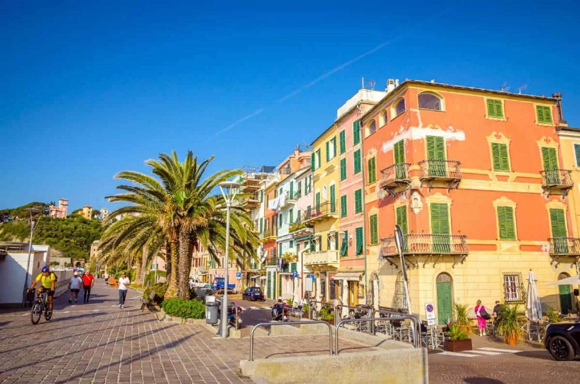 Una strada con edifici colorati, palme e persone che passeggiano.