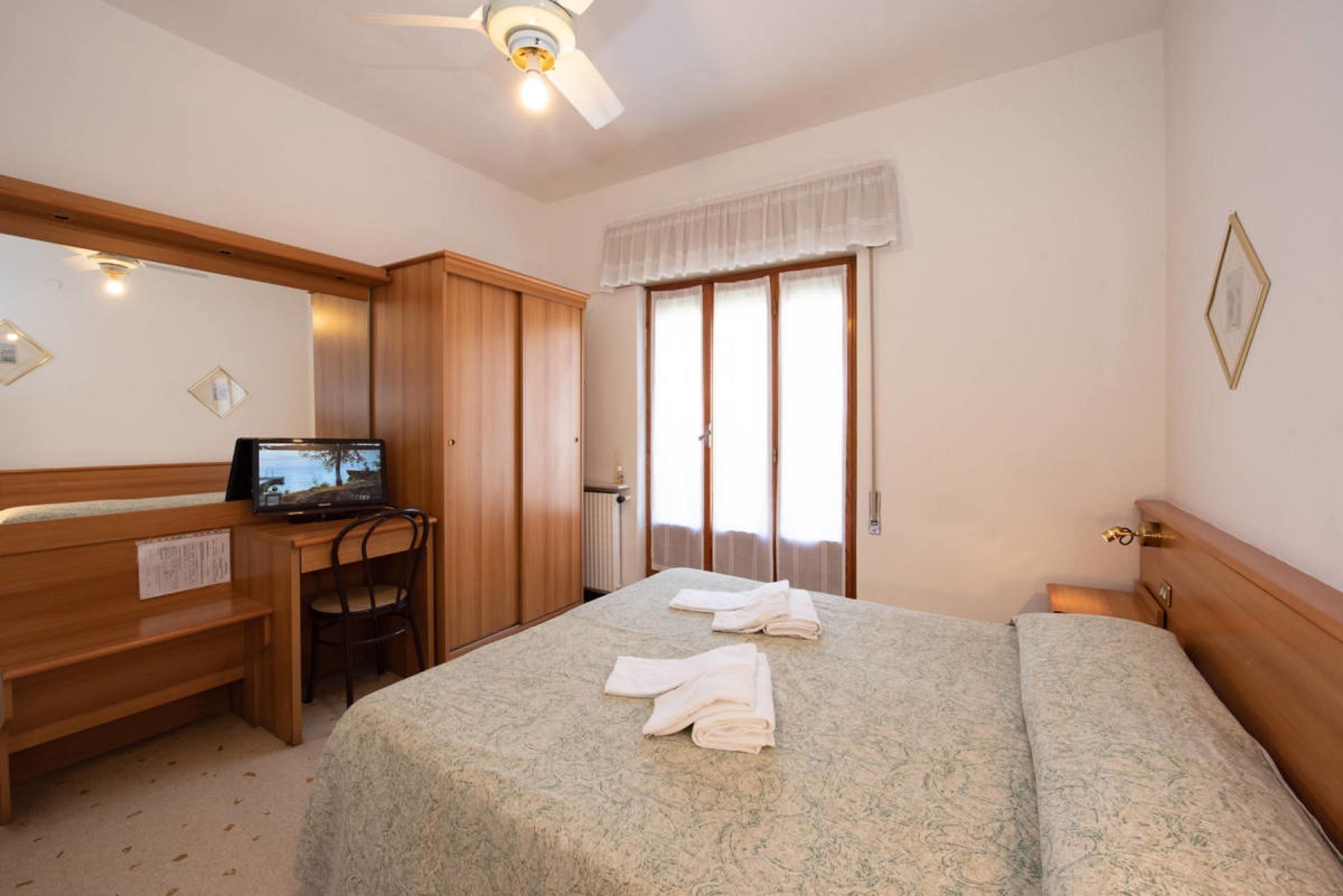 Una habitación de hotel con cama, escritorio con silla, televisor y ventana con cortinas.