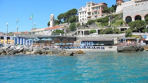Un pueblo costero con un puerto deportivo, sombrillas de playa y un edificio histórico con arcos.