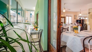 Un comedor con mesas dispuestas para una comida, un ventanal con vistas y una puerta que conduce a otra habitación.