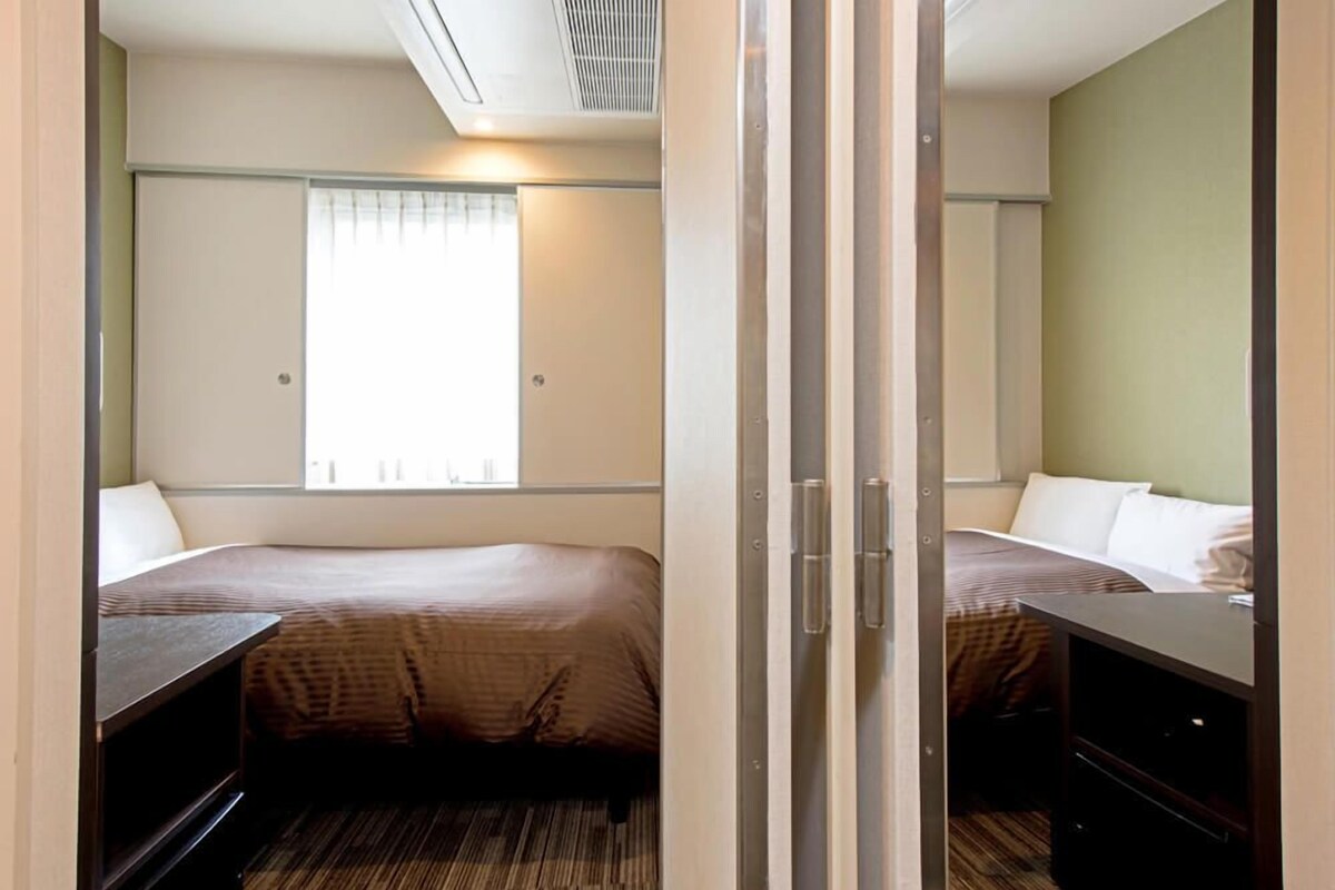 A hotel room with two beds, a window, and a sliding door.