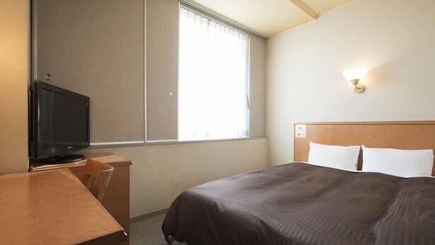 A hotel room with a bed, a desk, a television, and a window with blinds.