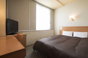 Une chambre d’hôtel équipée d’un lit, d’un bureau, d’une télévision et d’une fenêtre avec des stores.
