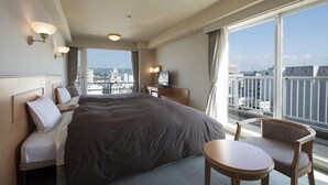 A hotel room with a large bed, a desk, a chair, and a view of the cityscape through large windows.