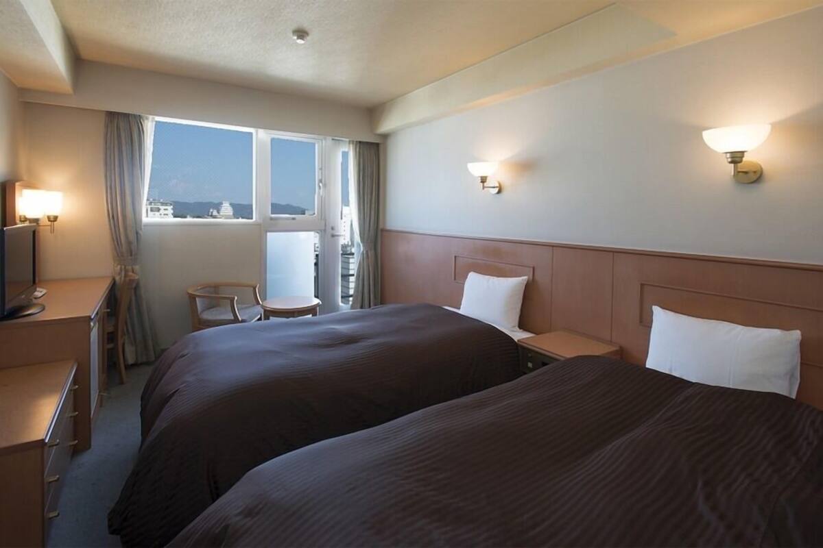 Een hotelkamer met twee bedden, een bureau, een stoel en een raam met uitzicht.