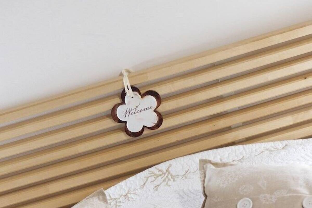 Un lit avec des oreillers de couleur beige ornés d’un motif représentant un récif corallien, une tête de lit en bois et une pancarte indiquant « Bienvenue ».