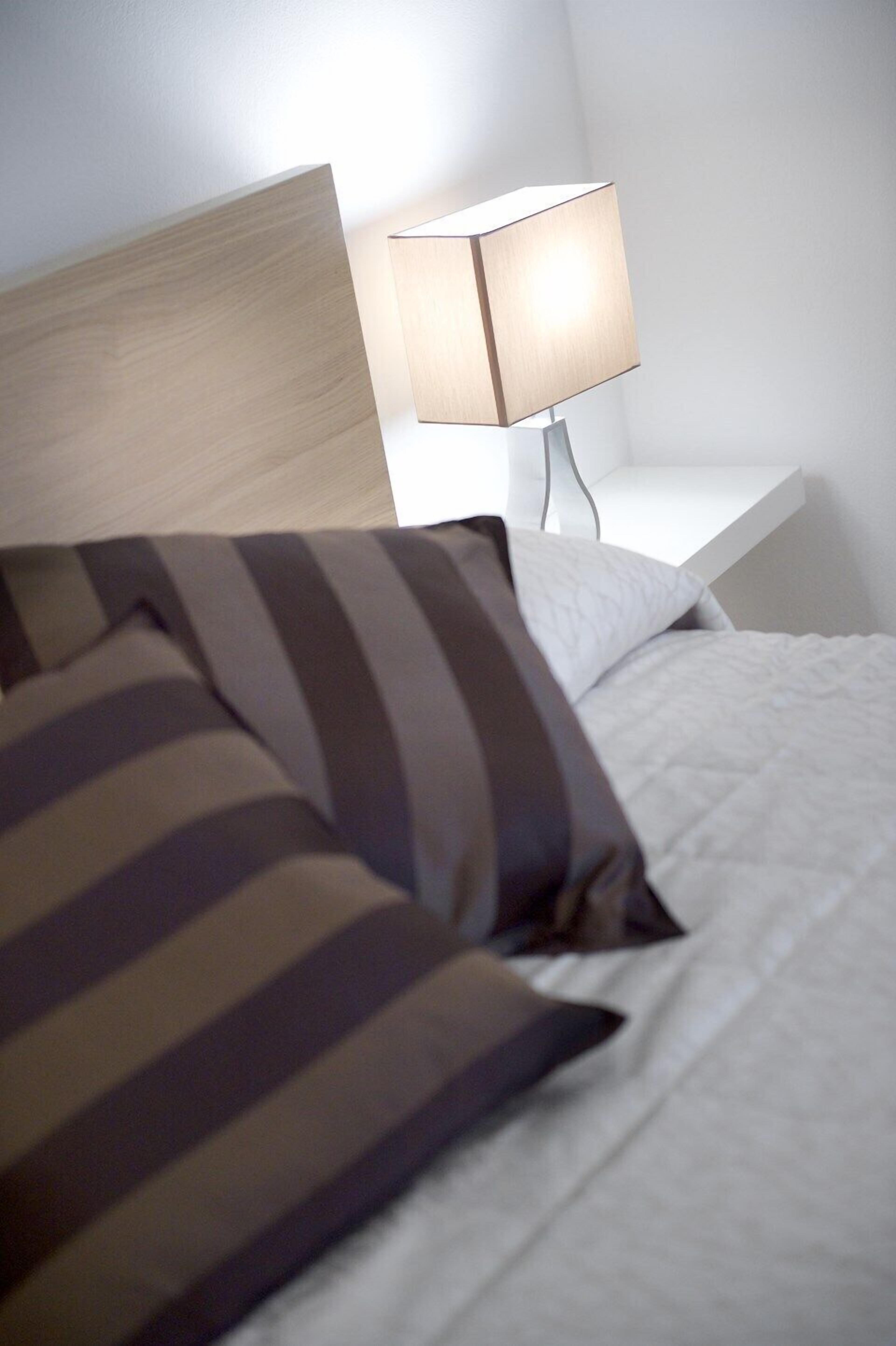 A bed with striped pillows and a bedside table with a lamp.