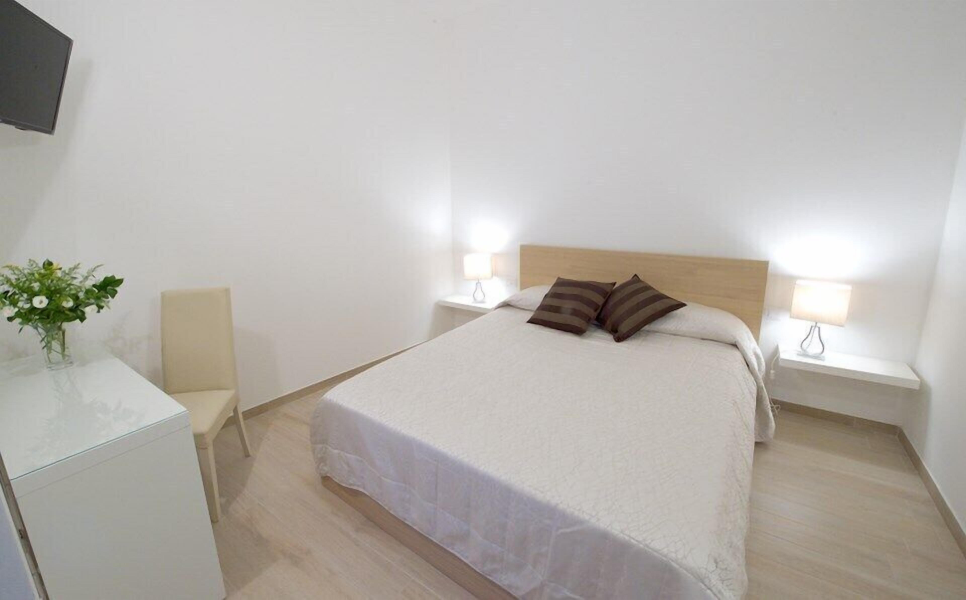 Una camera da letto ordinata con un letto, comodini, un tavolino, una sedia e un piccolo tavolo con un vaso di fiori.