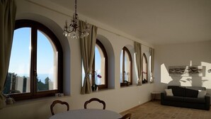 Una habitación con una mesa redonda, sillas, un sofá y ventanas arqueadas grandes con cortinas.