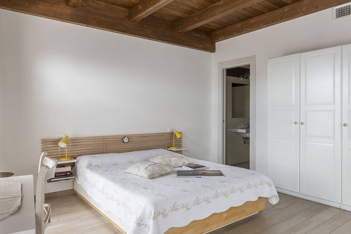 Une chambre à coucher avec un lit en bois, du linge de lit blanc, une table de chevet avec une lampe et une armoire.