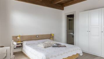 Un dormitorio con estructura de cama de madera, ropa de cama blanca, una mesita de noche con lámpara y un armario.