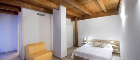 A bedroom with a wooden ceiling, a bed with a white bedspread, a nightstand, and a yellow chair.