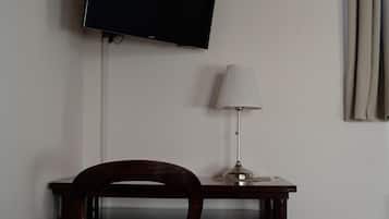 Ein Zimmer mit einem an der Wand montierten Flachbildfernseher, einem Schreibtisch mit Lampe und einem Sessel.