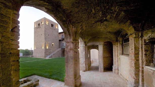 Un antiguo edificio de piedra con una torre, pasajes abovedados y un patio cubierto de césped.