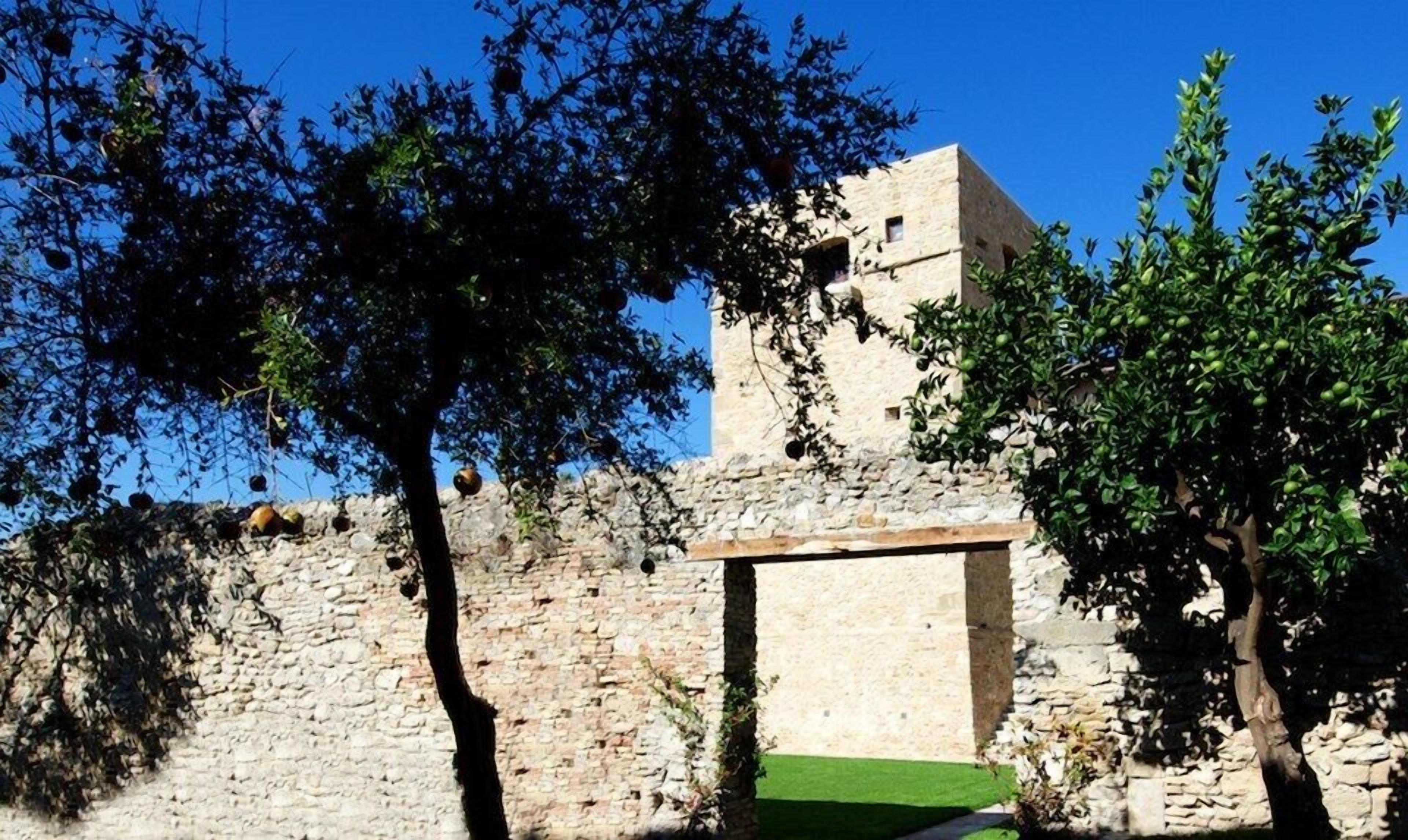A stone building with a tower, surrounded by trees and a stone wall.