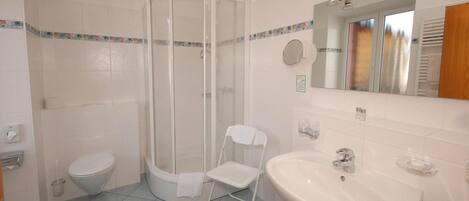Un baño con inodoro, ducha con puerta de vidrio, lavamanos y espejo.