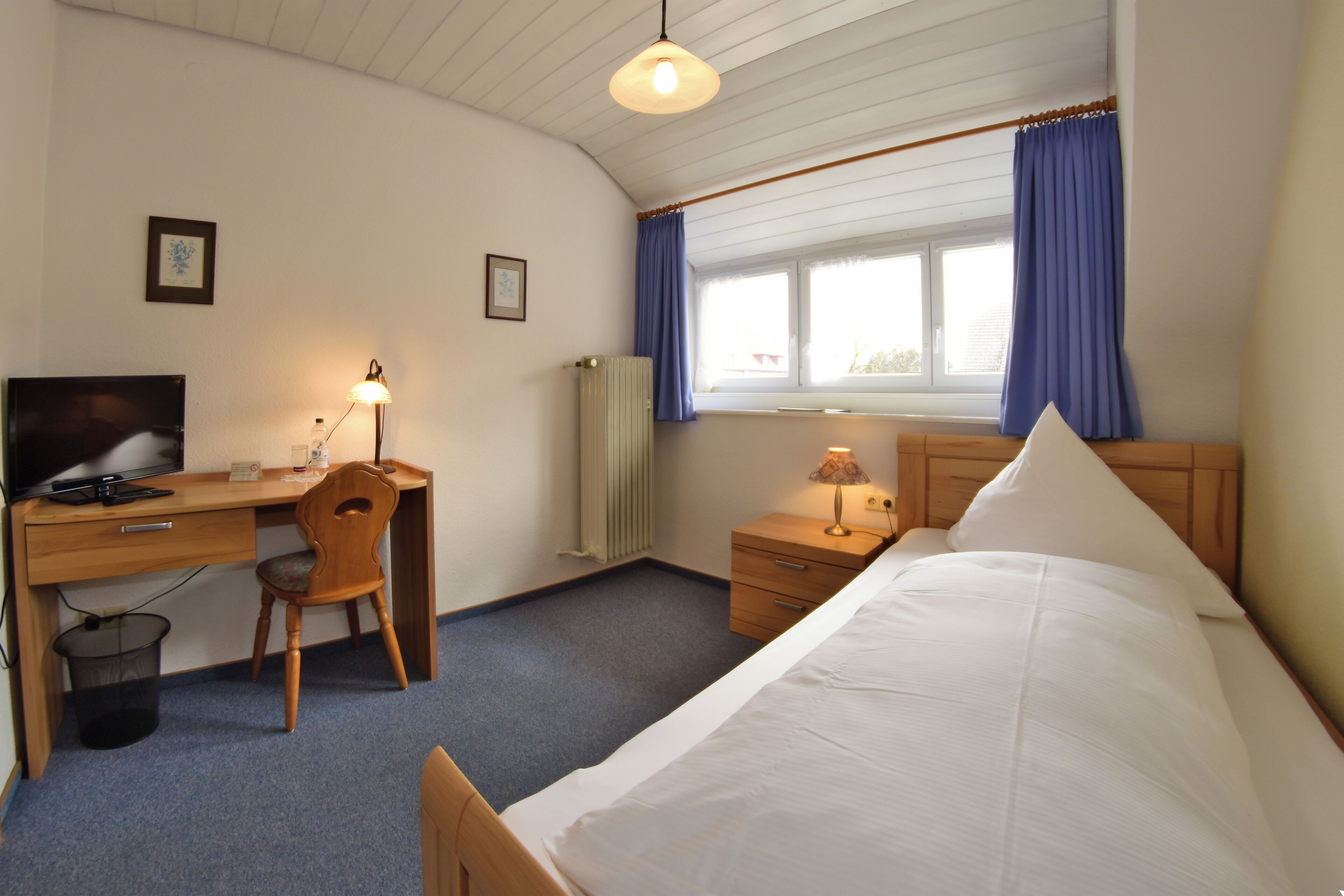 Une chambre à coucher avec un lit, un bureau avec une chaise, une télévision et une fenêtre avec des rideaux.
