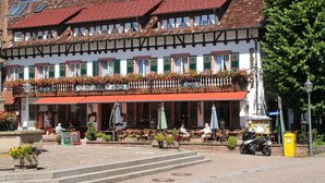 Ein traditionelles europäisches Gebäude mit einem Balkon, der mit Blumen geschmückt ist, Sitzgelegenheiten im Freien und einem Kopfsteinpflasterplatz.