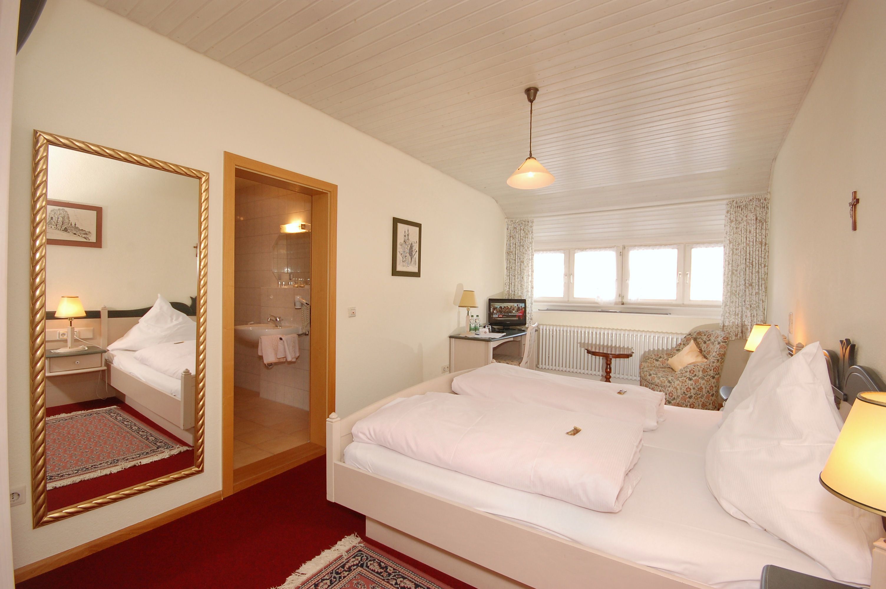 A bedroom with a large bed, a mirror, a desk, a chair, and a window.