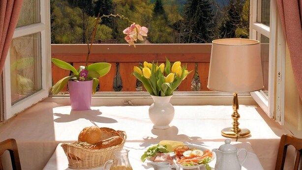 Ein Esstisch mit Panoramablick auf die Berge, ein Korbwäscher, eine Vase mit Blumen und verschiedene Frühstücksartikel.