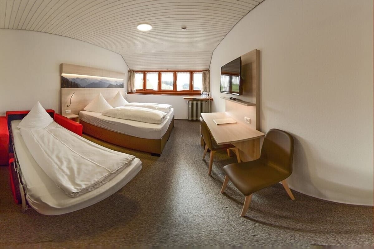 Et moderne hotelværelse med seng, skrivebord, stol, tv og et vindue med udsigt til bjerge.