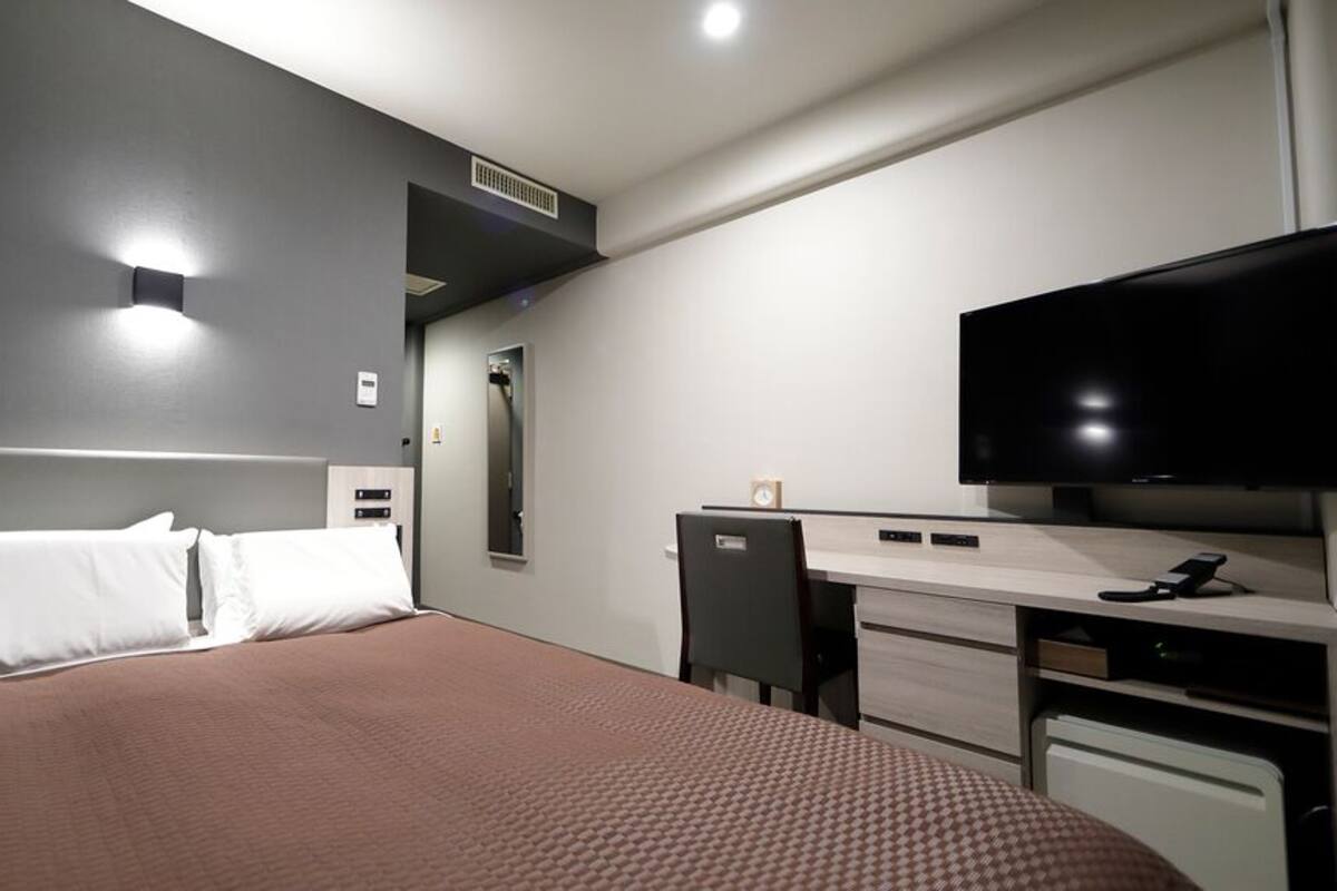 A hotel room with a bed, a desk, a television, and a mirror.