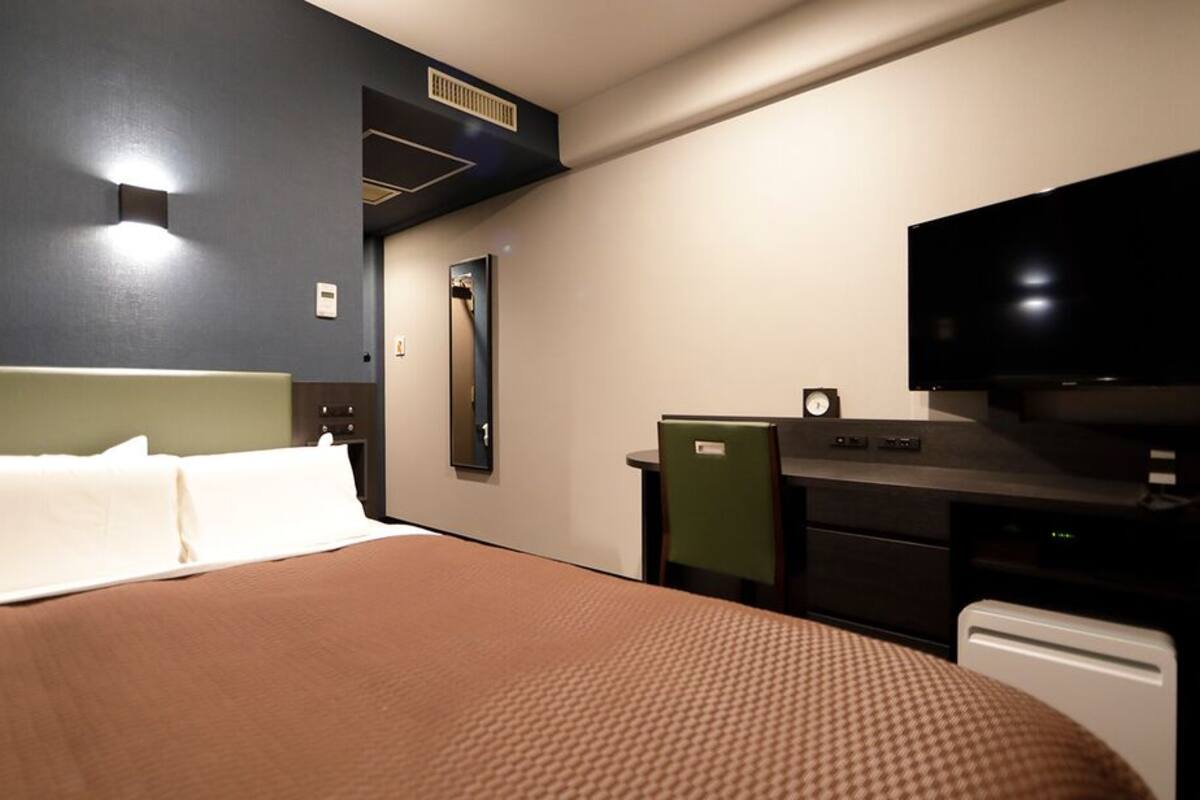 A hotel room with a bed, a desk with a television, a mirror, and a small clock.