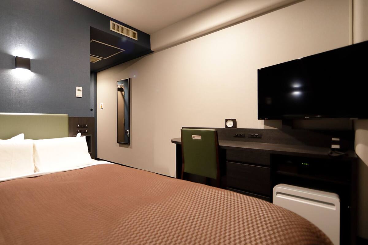 A hotel room with a bed, a desk, a television, and a mirror.