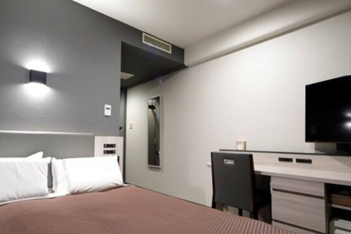 A modern hotel room with a bed, a desk, a chair, and a flat-screen TV.