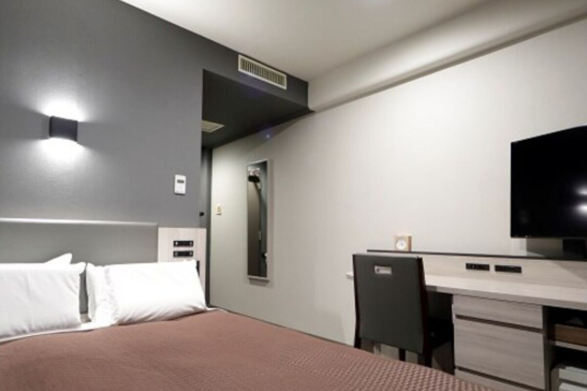 A modern hotel room with a bed, a desk, a chair, and a flat-screen TV.